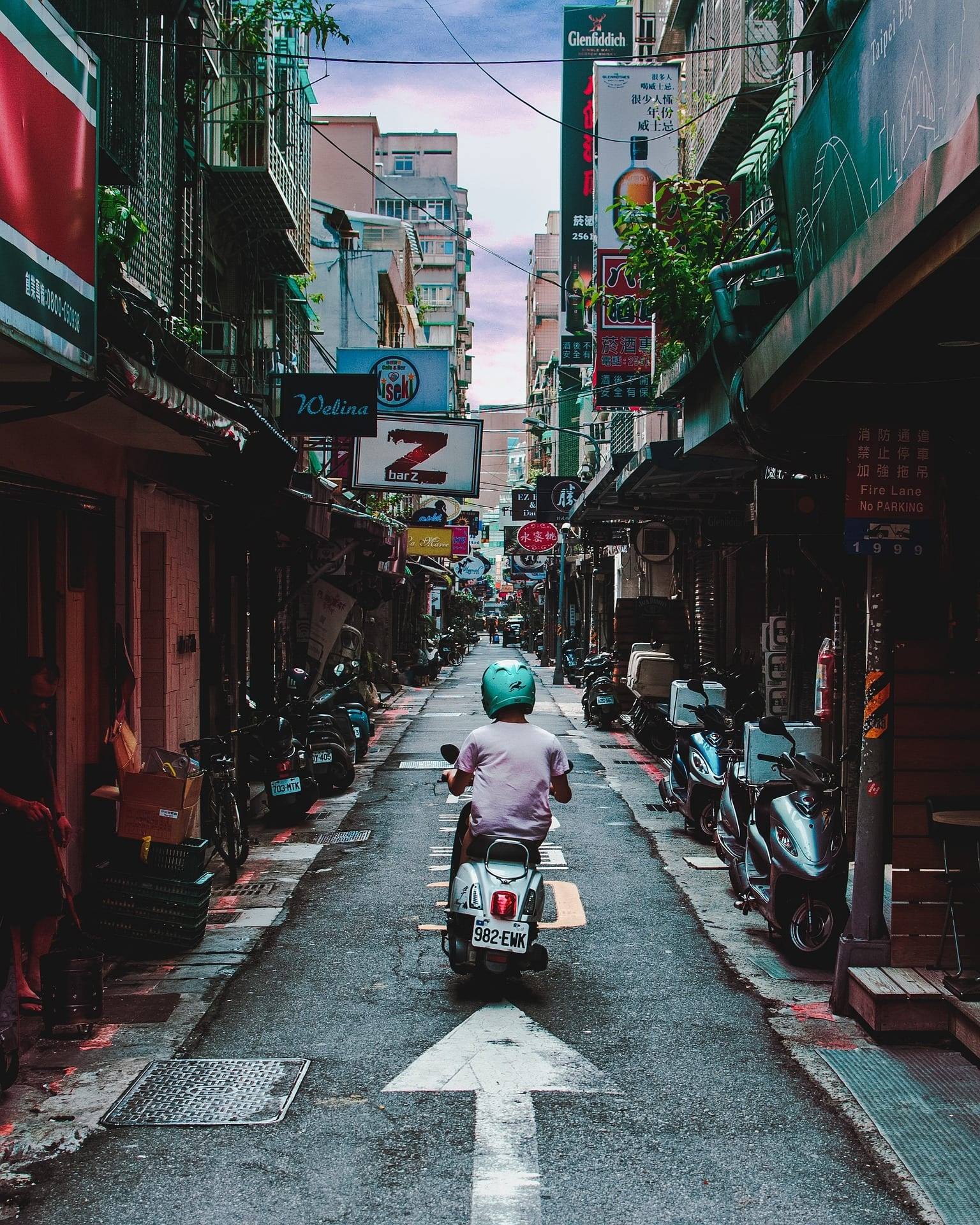 看板が並ぶ台湾の細い路地を走るスクーター。IOSTを買う人がBinanceなど海外の取引所に頼っている台湾の街並み